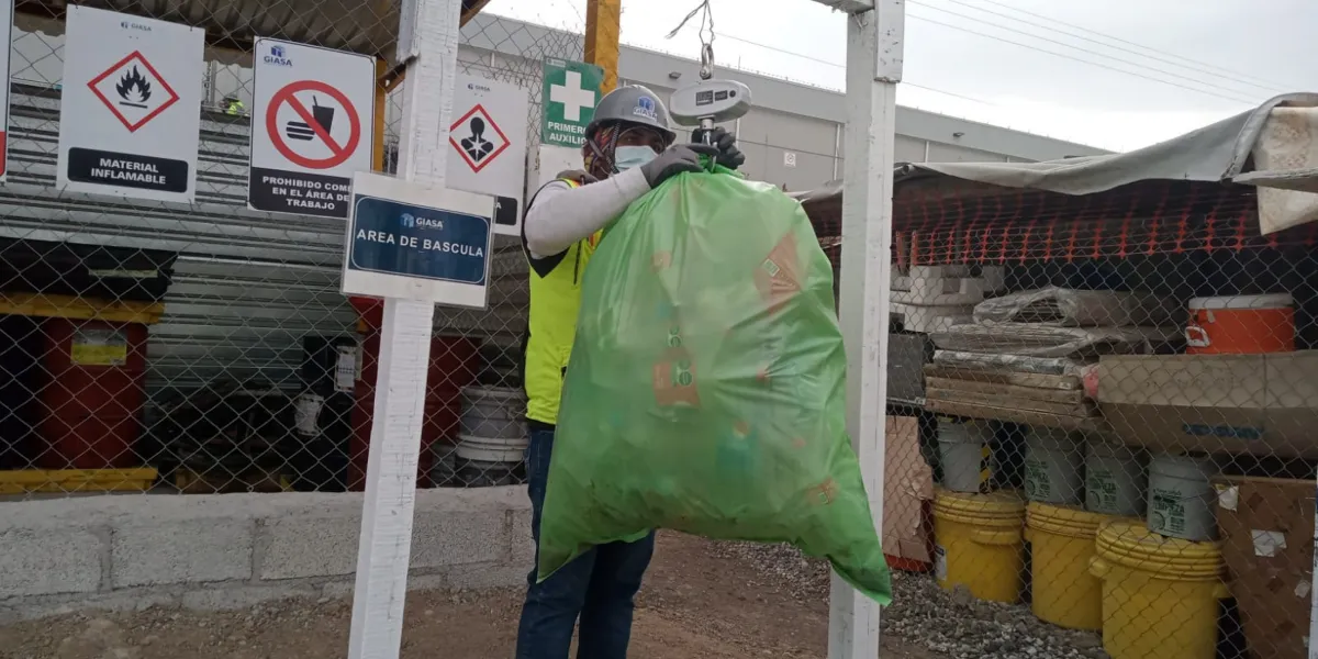 Operador de GIASA en zona de reciclaje pesando una bolsa verde con material recuperado, como parte del programa ambiental en obra.